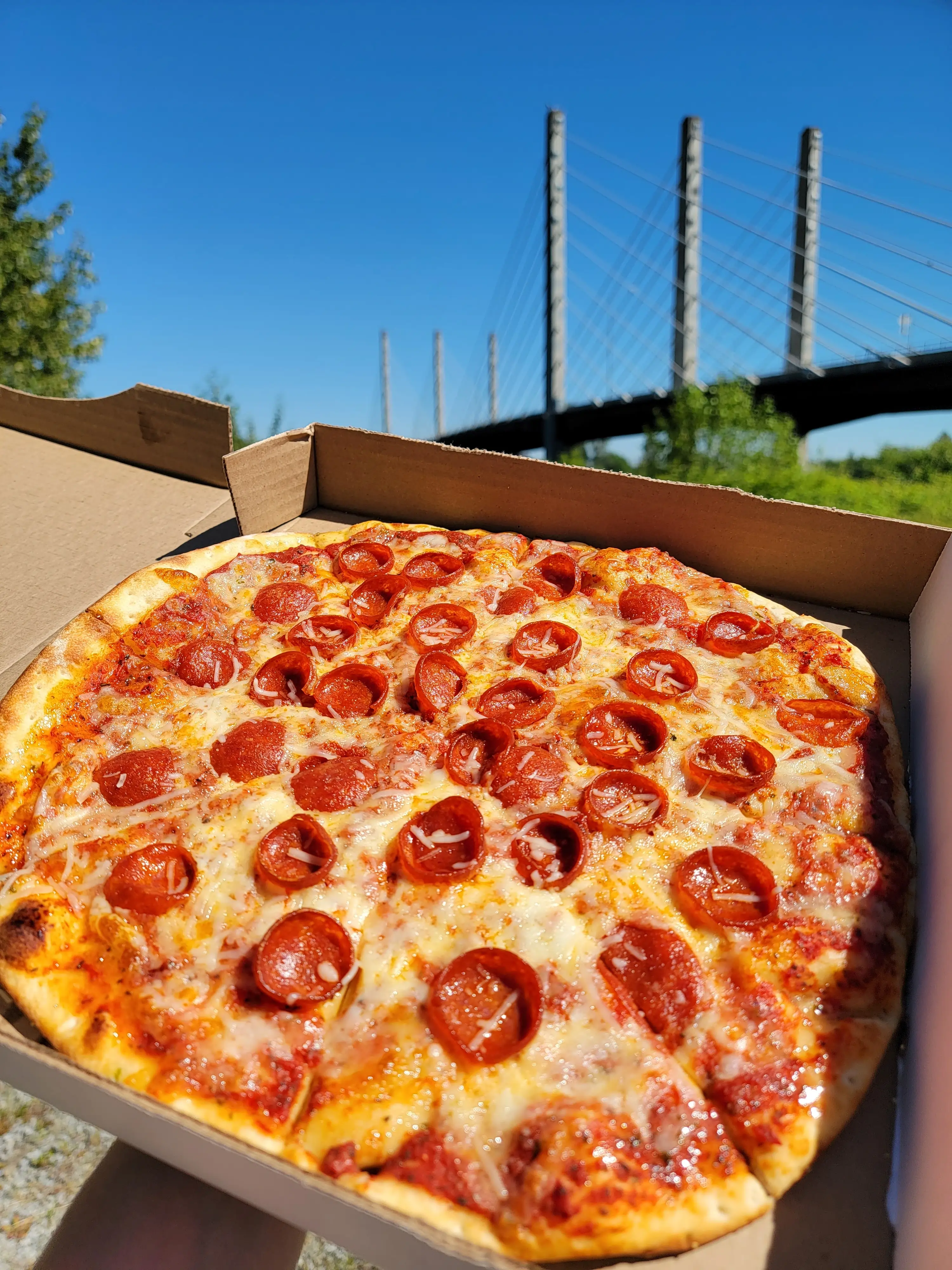 A dilicious cup and char pepperoni pie with a bridge in the distance.